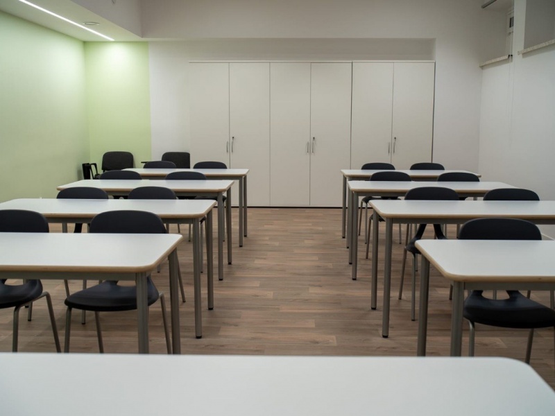 Klasa z białymi biurkami i ciemnymi krzesłami.