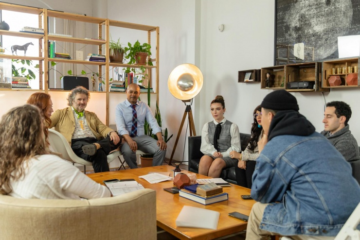 Na zdjęciu jest pokazana grupa, która siedzi dookoła stołu i razem ze sobą rozmawiają.