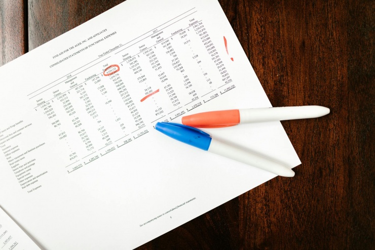 Na zdjęciu jest na stole położony dokument na nim jest coś podkreślone, a  na tym dokumencie znajdują się dwa mazaki w kolorze niebieskim oraz pomarańczowym.