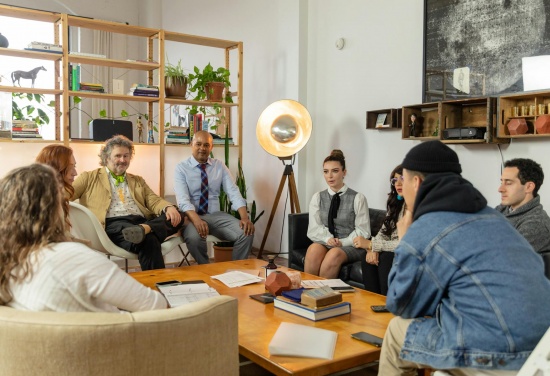 Na zdjęciu jest pokazana grupa, która siedzi dookoła stołu i razem ze sobą rozmawiają.