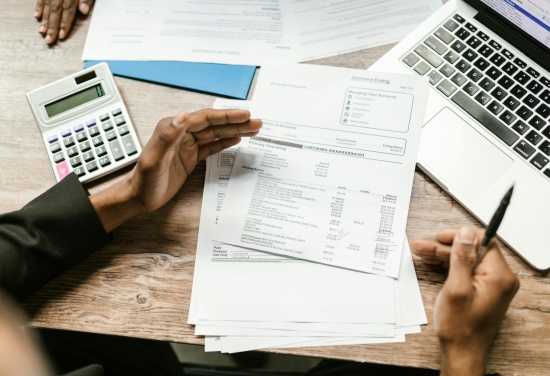 Osoba przygląda się garścią dokumentów trzymając w prawej ręce długopis